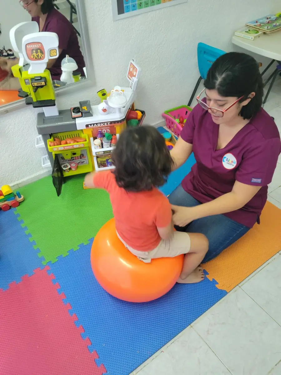 Terapeuta trabajando con una niña sentada sobre una pelota de estimulación